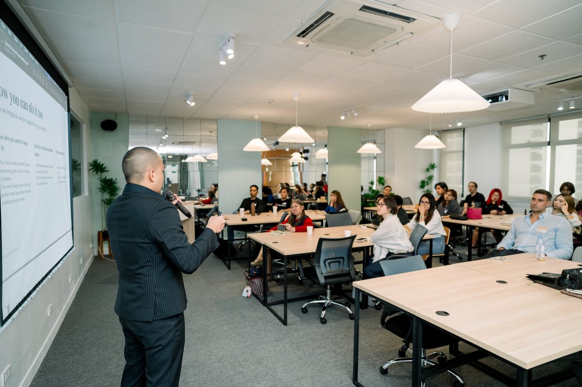 Professional man in dark suit presenting to a room full of seated employees at a modern office conference area with large display screen