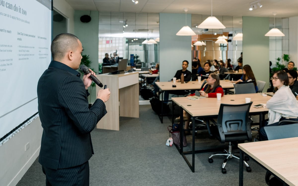 Professional man in dark suit presenting to seated employees at modern office with white tables and green walls